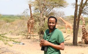 Ali on sight in Kenya with giraffes in the background